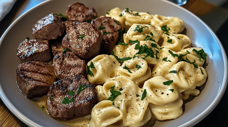 A cozy dinner plate of Garlic Butter Steak Bites and Creamy Alfredo Tortellini with rustic table setting.
