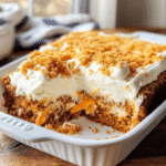 Moist carrot poke cake in a farmhouse baking dish with cream cheese filling and fluffy frosting, styled on a rustic table