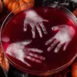 Spooky Halloween party punch in a clear bowl with fruit and gummy worms, styled with pumpkins and spider webs.
