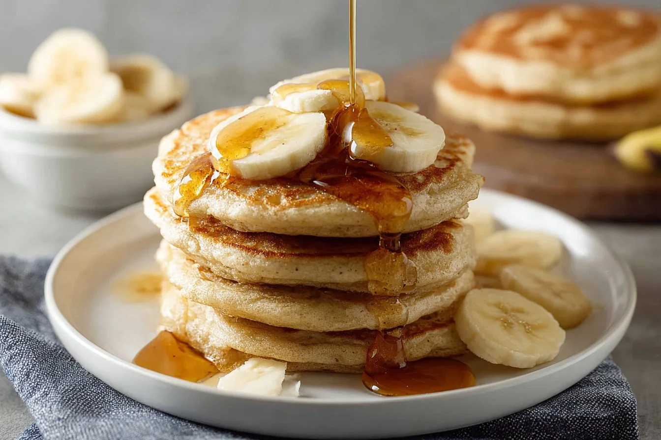 Stack of fluffy banana pancakes topped with syrup and sliced bananas