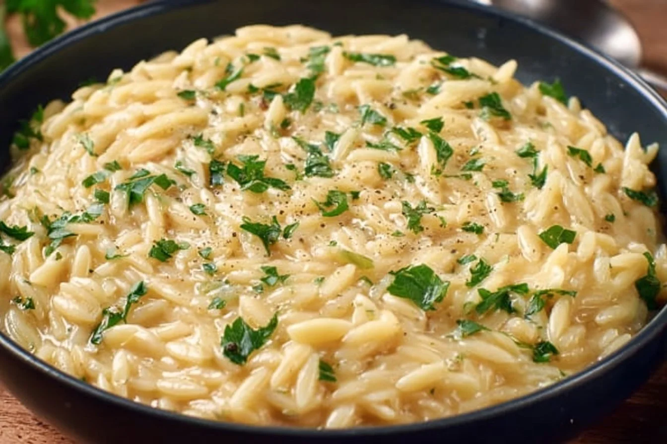 Creamy garlic parmesan orzo with herbs in a bowl, garnished with parmesan cheese.