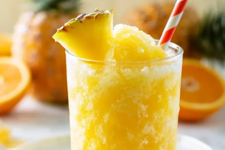 Refreshing pineapple slush drink in a tall glass with ice and garnished with pineapple slices.